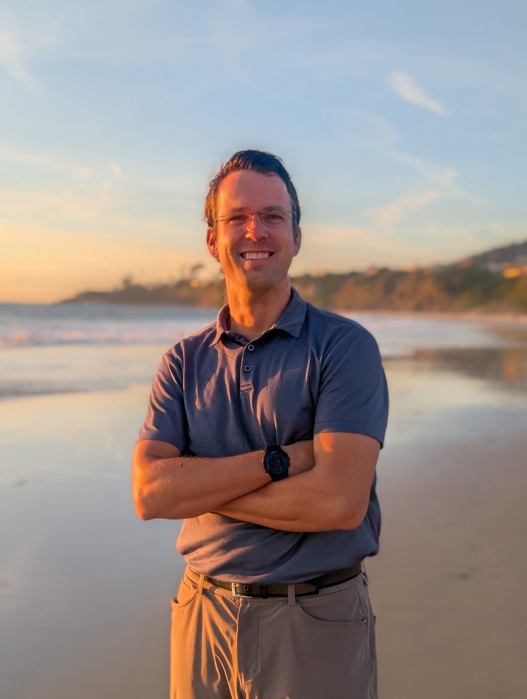 Matthew Siljander on the beach at sunset, arms crossed, smiling